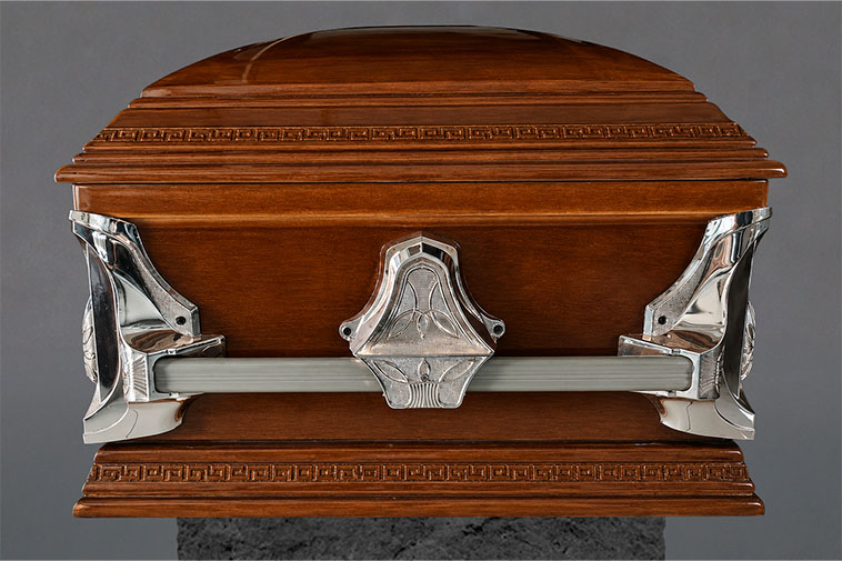 Detalle frontal de ataúd Premium con diseño curvo, madera pulida y asas metálicas decorativas para servicios funerarios.