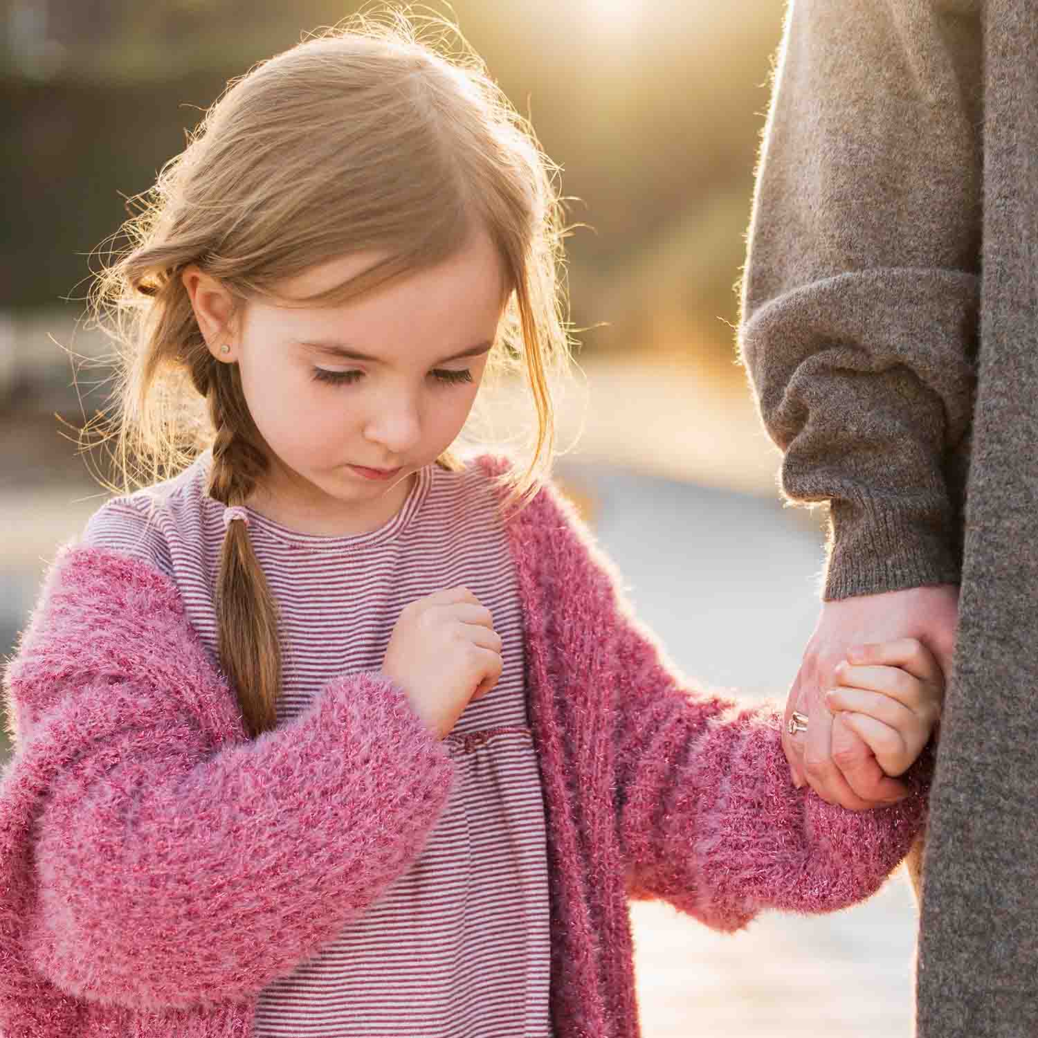 Niña tomando la mano de su madre y con la cabeza agachada y su mirada al suelo.